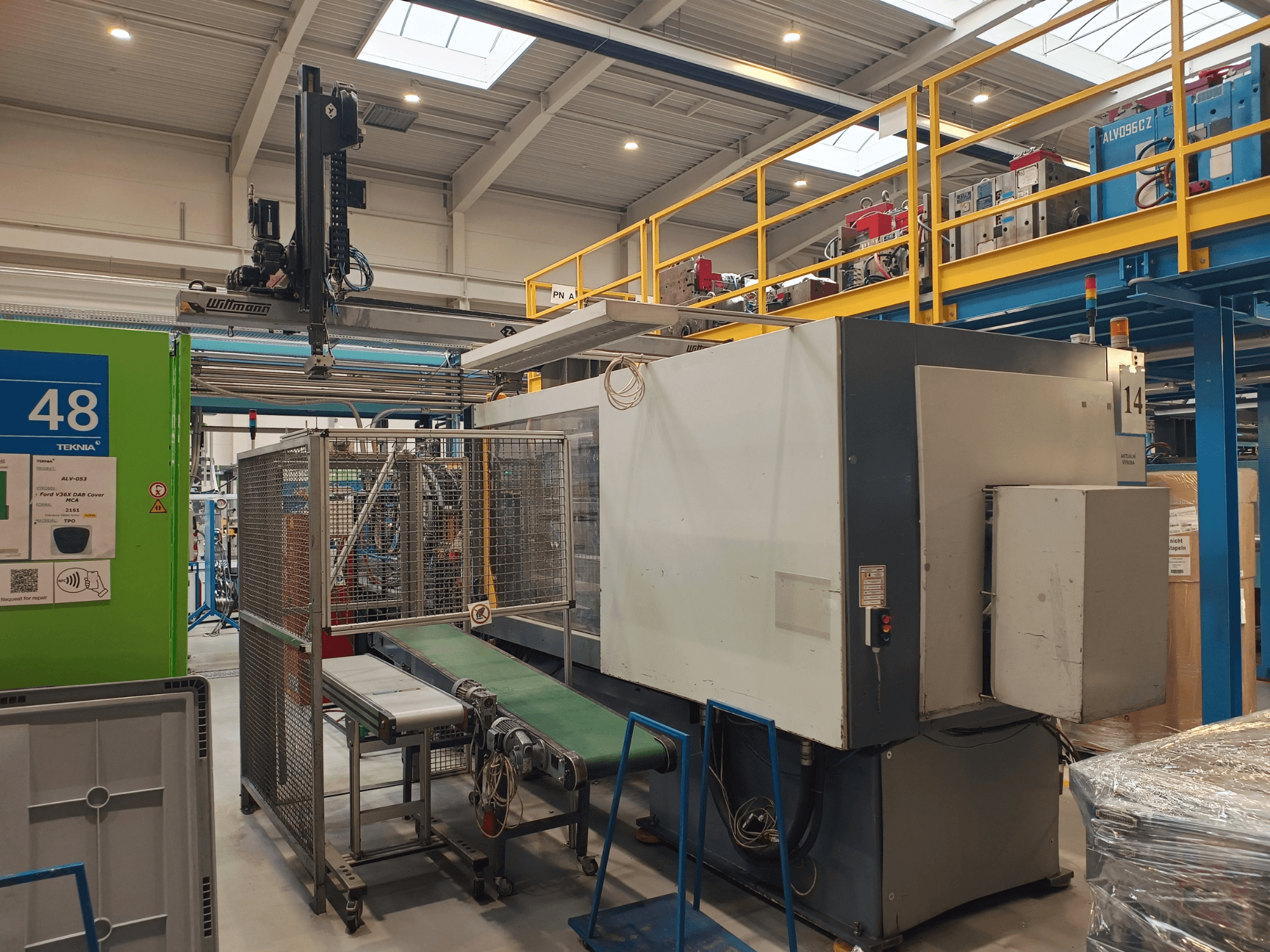 Industriell automationsutrustning med grön transportör, märkt "48", och traverskran; sidovy av maskin på fabriksgolv.